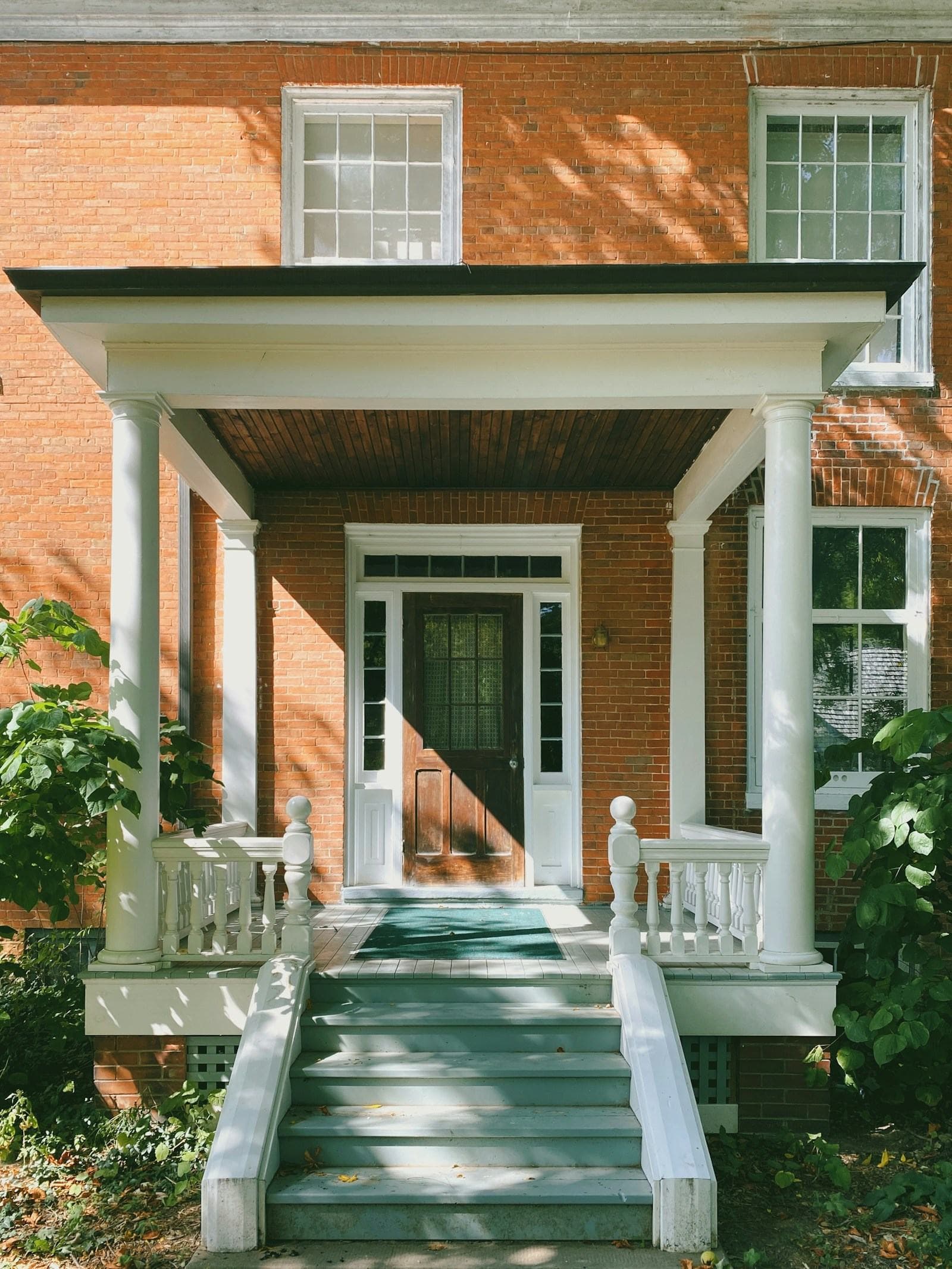 Columned front portico with white balustrades and a wood front door on a red brick home